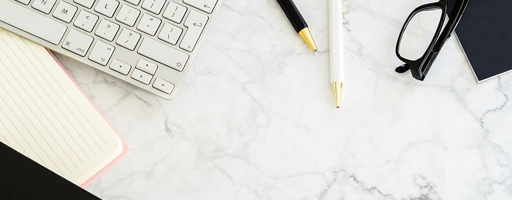 Keyboard, pens, glasses and a notepad on a marble desk